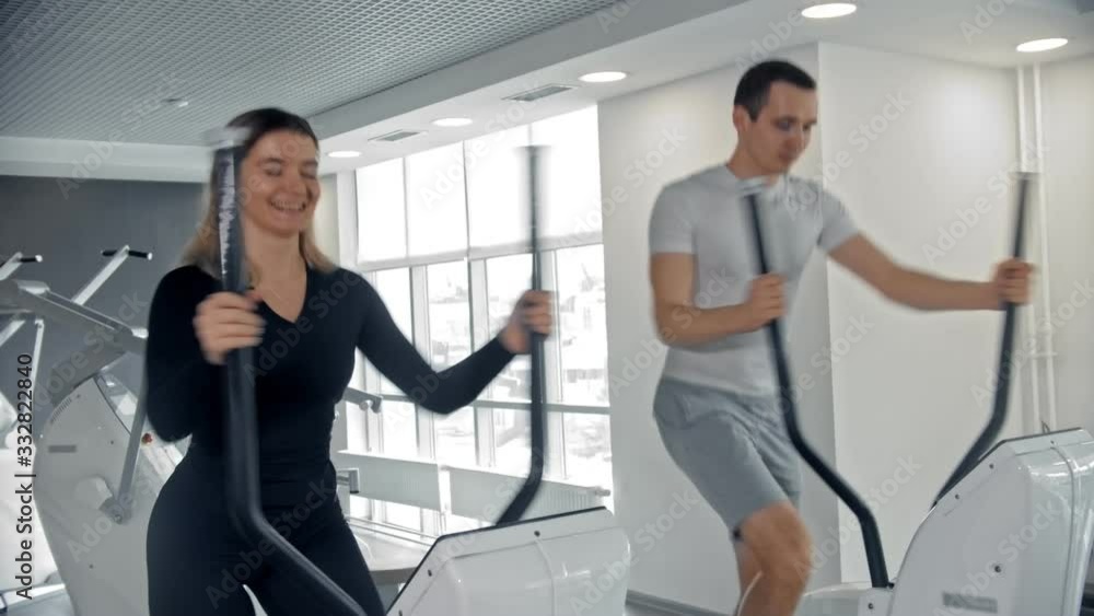 Sportive man and woman training their legs on exercise bike in white modern gym indoors Sportive man and woman training their legs on exercise bike in white modern gym indoors