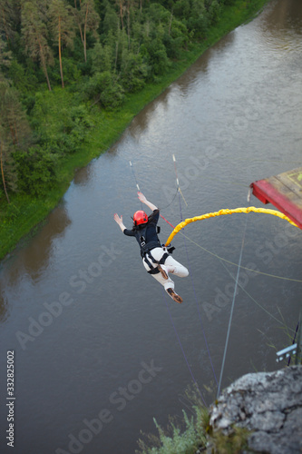 Girl, tied on a safety rope, jumping from a great height falls into a deep canyon against the background of a river. Ropejumping.