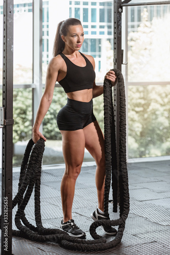 Portrait of fitness woman with battle rope in modern gym