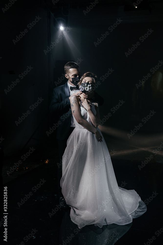 The bride and groom in wedding dresses and in black medical masks decorated with fresh flowers The bride and groom in wedding dresses and in black medical masks decorated with fresh flowers