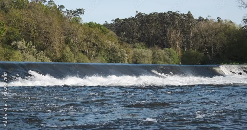 Beautiful fast flowing river in spring with water gushing over weir and tall trees in background. River Ave in Portugal. Beautiful fast flowing river in spring with water gushing over weir and tall trees in background. River Ave in Portugal.