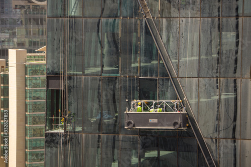 Group of workers cleaning the windows of a high rise building, dangling from secure ropes. Washing the windows of a skyscraper, view of clean and dirty windows.