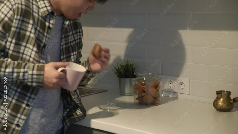 Close up of Asian man taking a cookie and drinking coffee at home in the kitchen. Close up of Asian man taking a cookie and drinking coffee at home in the kitchen.