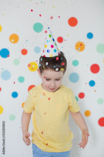 Toddler boy in the birthday hat on a background of wall with colorful circles