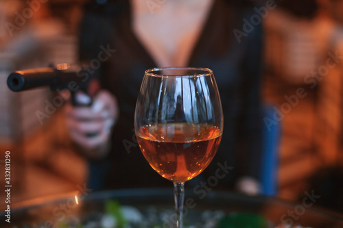 Glass of alcohol close up. Behind him the silhouette of a woman with a gun.