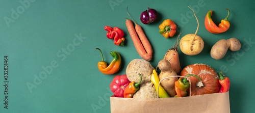 Trendy ugly organic vegetables. Assortment of fresh eggplant, onion, carrot, zucchini, potatoes, pumpkin, pepper in craft paper bag over green background. Top view. Cooking ugly food concept. Non gmo photo