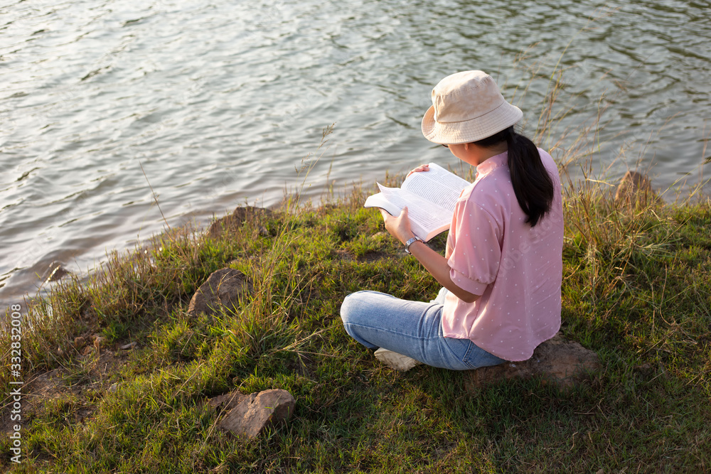 A young woman reading a book on the waterfront in the evening