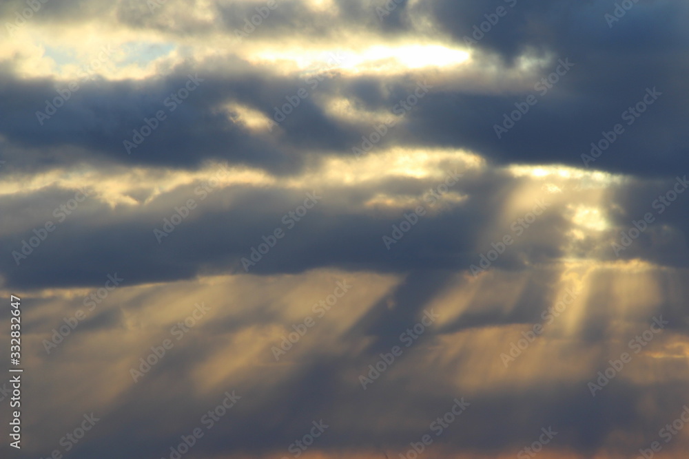 The sun at sunset or dawn behind the clouds, shines through. The sun's rays in the sky. The sun at sunset or dawn behind the clouds, shines through. The sun's rays in the sky.