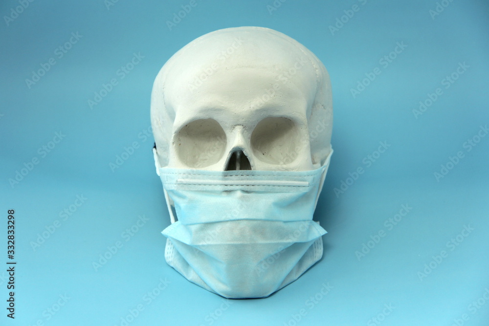 White human skull made of gypsum with a medical mask on a blue background. The concept of a pandemic, medicine and coronovirus. White human skull made of gypsum with a medical mask on a blue background. The concept of a pandemic, medicine and coronovirus.