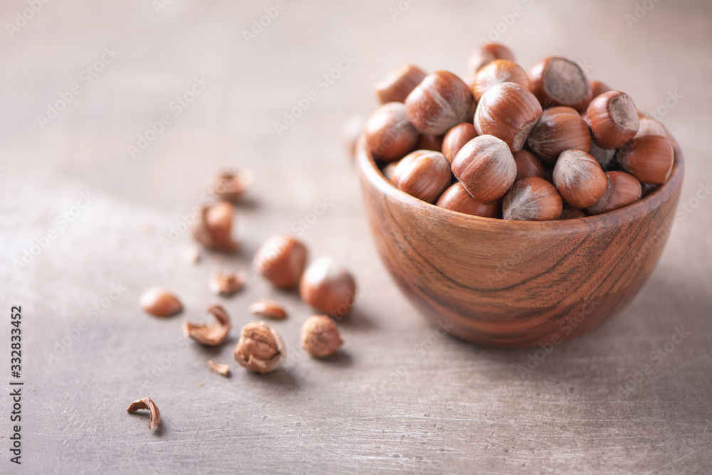 Fototapeta premium Hazelnuts in wooden bowl on wood textured background. Copy space. Superfood, vegan, vegetarian food concept. Macro of hazelnut, selective focus. Healthy snack.