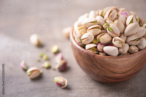 Green pistachio nuts in wooden bowl on wood textured background. Copy space. Superfood, vegan, vegetarian food concept. Macro of pistachio nut texture, selective focus. Healthy snack. photo