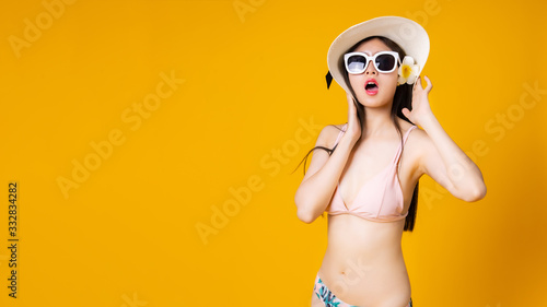 Beautiful,Sexy asian girl standing on yellow background in a colors bikini and smiling.Summer vocation happy trip concept.