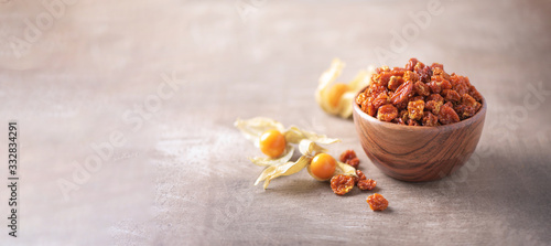 Dried physalis in wooden bowl and fresh berries on wood textured background. Copy space. Superfood, vegan, vegetarian food concept. Macro of inca berries, selective focus. Healthy snack.