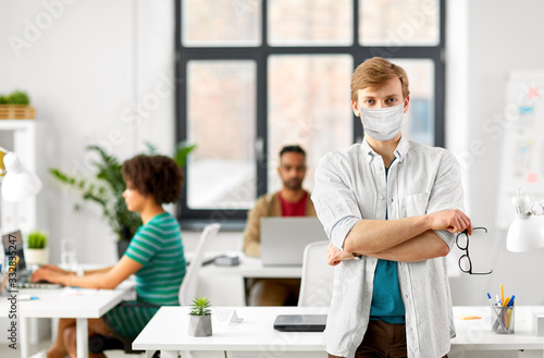 business and people concept - man with glasses wearing protective medical mask for protection from virus disease at office