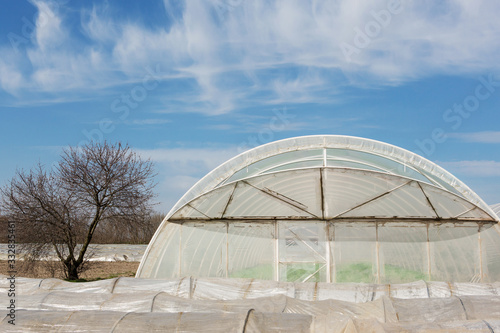 tunnel low greenhouses and a large greenhouse stand in rows on farmland, industrial cultivation of early vegetables, in the background a blue sky
