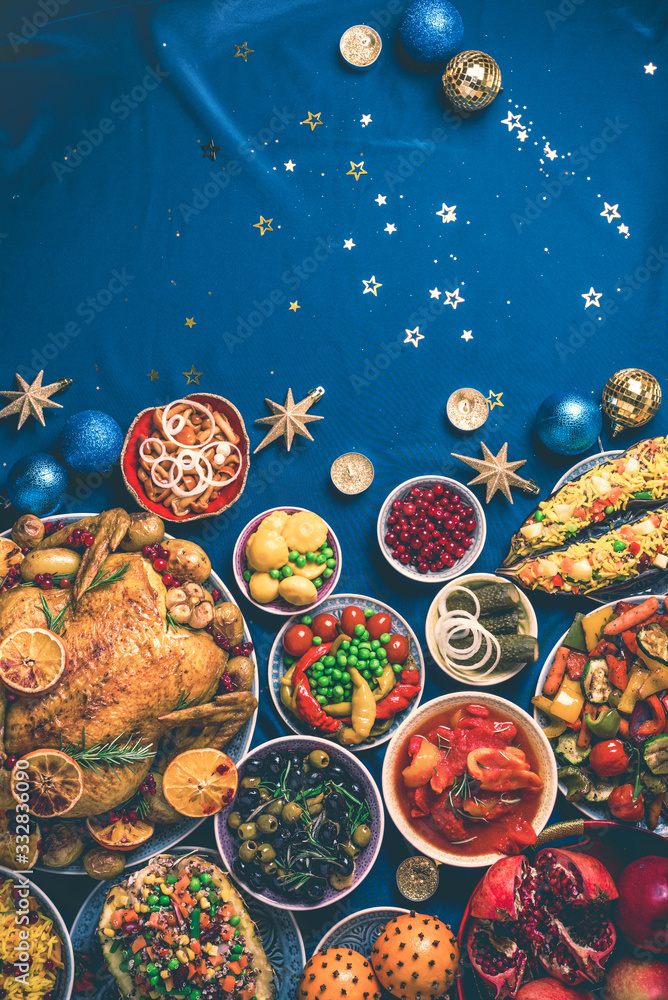 Roasted Christmas turkey with orange slices, cranberries, garlic, festive decoration, candles, tangerine, pomegranate, golden cultery, star glitter sparkles on blue background. Top view, copy space Roasted Christmas turkey with orange slices, cranberries, garlic, festive decoration, candles, tangerine, pomegranate, golden cultery, star glitter sparkles on blue background. Top view, copy space