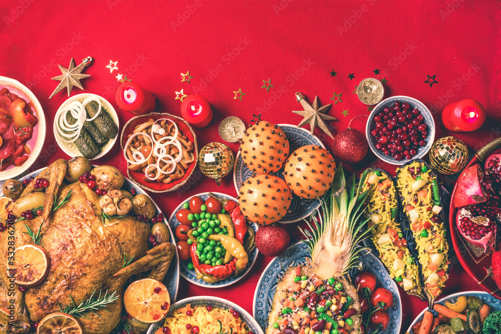 Festive family dinner. Top view. Roasted Christmas chicken with orange slices, cranberries, garlic, festive decoration, candles, tangerine, pomegranate, golden cultery, star glitter sparkles on red