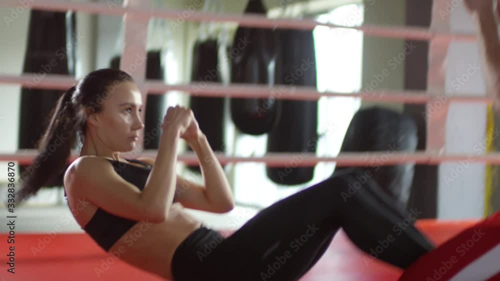 Athletic female boxer doing sit ups and practicing punches with assistance of male trainer during workout in ring Athletic female boxer doing sit ups and practicing punches with assistance of male trainer during workout in ring