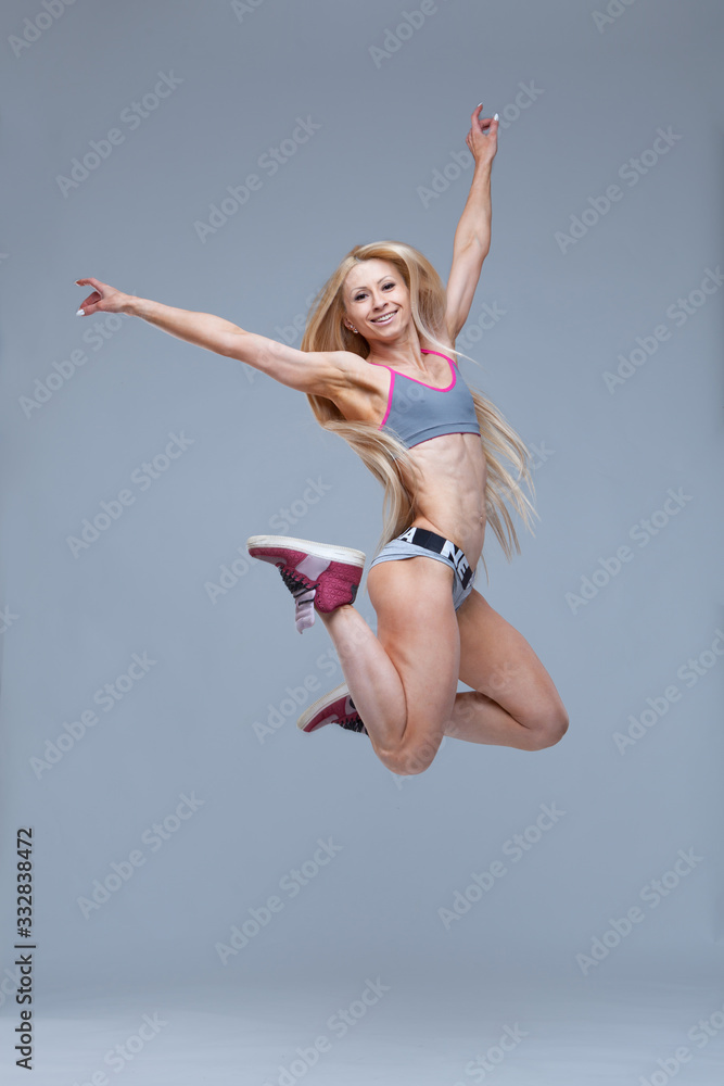 Fototapeta premium Full length portrait of a happy smiling fitness girl jumping high isolated on grey background