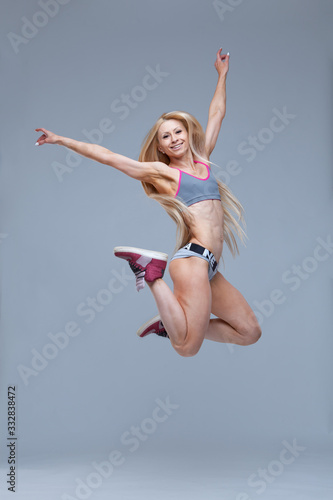 Full length portrait of a happy smiling fitness girl jumping high isolated on grey background