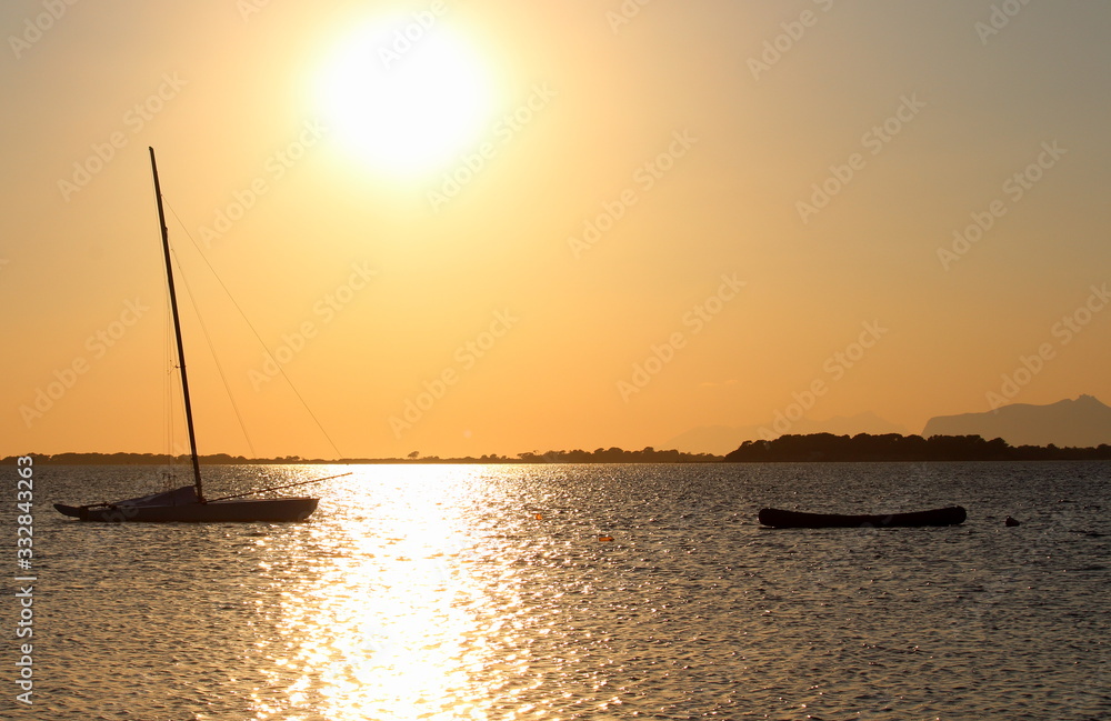 sailboat and canoe moored on the sea at sunset and headland on the background