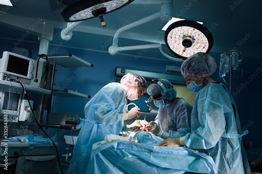 Fototapeta In the hospital operating room. An international team of professional surgeons and assistants works in a modern operating room. Professional doctors celebrate successfully saved lives.
