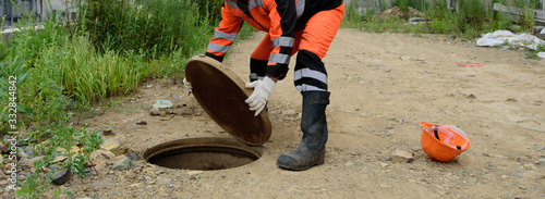 A worker in uniform lifts the sewer header cover.