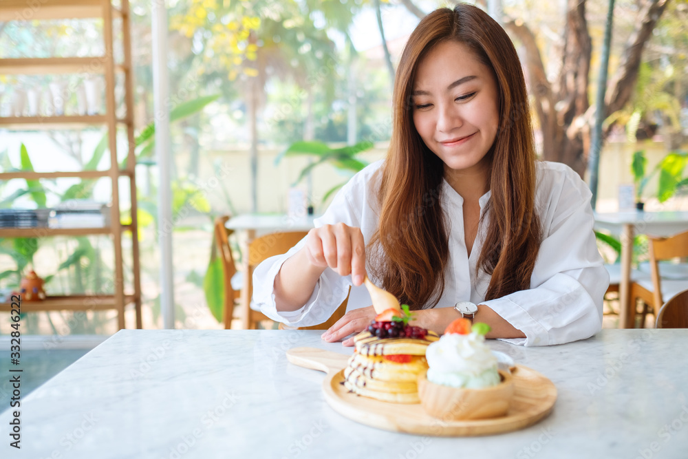 A beautiful asian woman eating ice cream and a mixed berries pancakes with whipped cream by wooden spoon