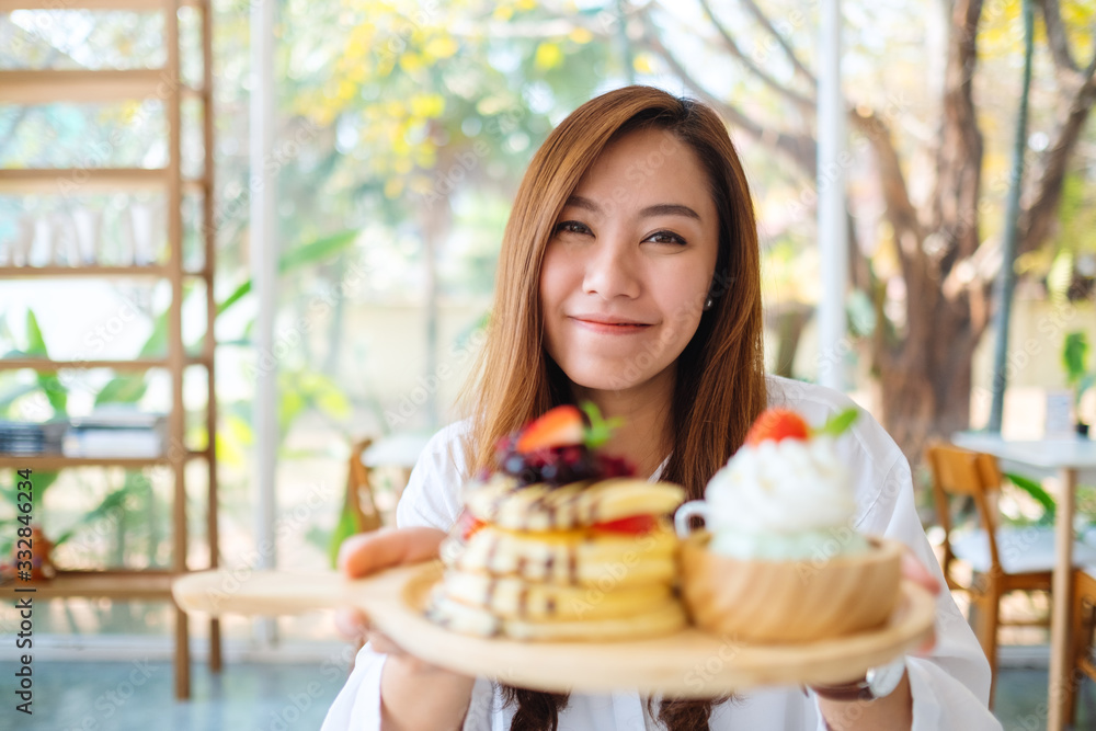 A beautiful asian woman holding and showing a plate of pancakes with ice cream and whipped cream in cafe A beautiful asian woman holding and showing a plate of pancakes with ice cream and whipped cream in cafe