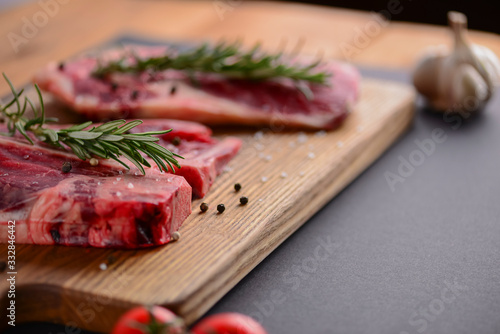 Fresh raw steak on wooden cutting board over black background with spices, top view.