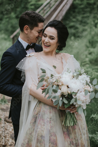 Smiling bride and groom spending time together. Posing on the mountain hills background. Dressed in white dress beautiful blonde caucasian bride and handsome groom. Hugs, kissess and enjoy the company