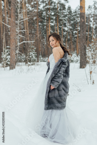 a beautiful girl in a wedding dress stands in a winter pine forest © Евгений Александров