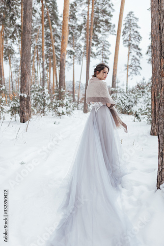 a beautiful girl in a wedding dress stands in a winter pine forest