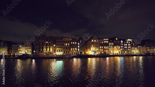 Canal of Amsterdam at night with reflection of illuminated houses in water, Netherlands. Beautiful old European city view.