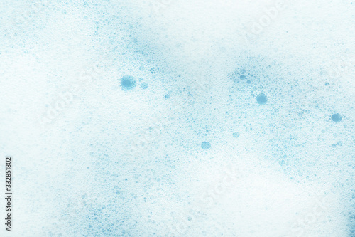 Foamy texture with bubbles on blue background. Moisturizing or cleansing cosmetics foam backdrop. Cosmetic product sample of mousse, shampoo or soap. Skincare, cosmetology and beauty concept