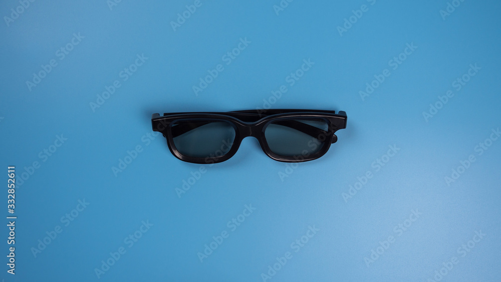 Black 3D glasses for watching a movie on a blue background. Flatlay