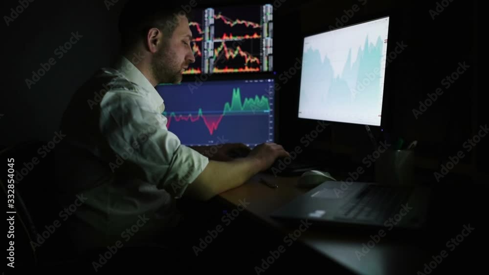 Stockbroker in white shirt is working in a dark monitoring room with display screens. Stock Exchange Trading Forex Finance Graphic Concept. Businessmen trading stocks online. Stockbroker in white shirt is working in a dark monitoring room with display screens. Stock Exchange Trading Forex Finance Graphic Concept. Businessmen trading stocks online.