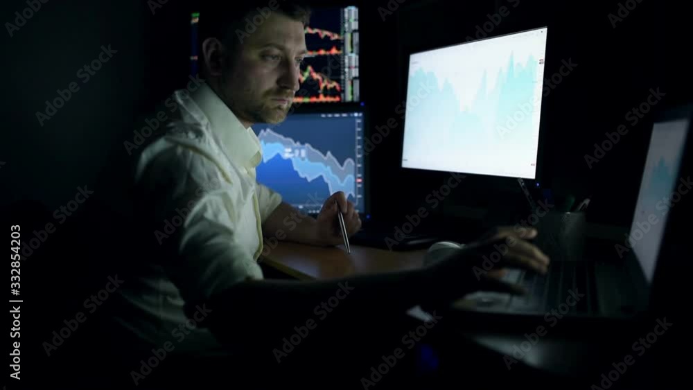 Stockbroker in white shirt is working in a dark monitoring room with display screens. Stock Exchange Trading Forex Finance Graphic Concept. Businessmen trading stocks online. Stockbroker in white shirt is working in a dark monitoring room with display screens. Stock Exchange Trading Forex Finance Graphic Concept. Businessmen trading stocks online.