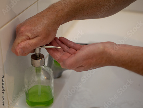 Man's hands are pressing the green liquide soap to wash his hands