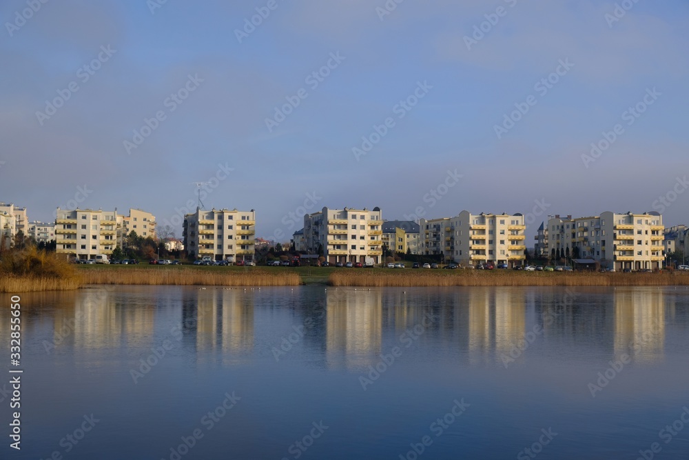 An estate of identical apartment blocks on the lake and its reflection in water, on the outskirts of the city. Idyllic view with blue sky and blue water. Gdansk South, Zakoniczyn, Poland