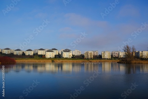 An estate of identical apartment blocks on the lake and its reflection in water, on the outskirts of the city. Idyllic view with blue sky and blue water. Gdansk South, Zakoniczyn, Poland