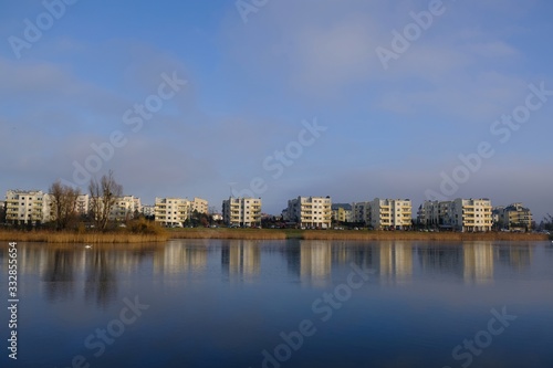 An estate of identical apartment blocks on the lake and its reflection in water, on the outskirts of the city. Idyllic view with blue sky and blue water. Gdansk South, Zakoniczyn, Poland