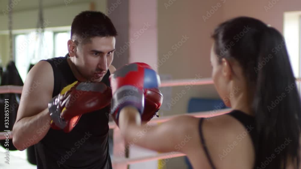 Professional male coach holding focus mitts while female boxer in gloves hitting them during training in the ring Professional male coach holding focus mitts while female boxer in gloves hitting them during training in the ring