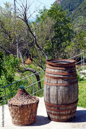 Old oak barrel for aging wine and glass and straw demijohn for storing wine on a farm           © andrea