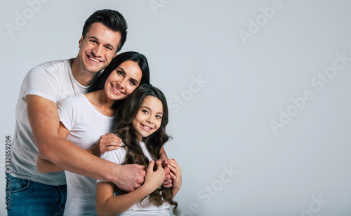 Beautiful excited and the funny family team is posing and pointing in a white t-shirt while they isolated on white background in studio.
