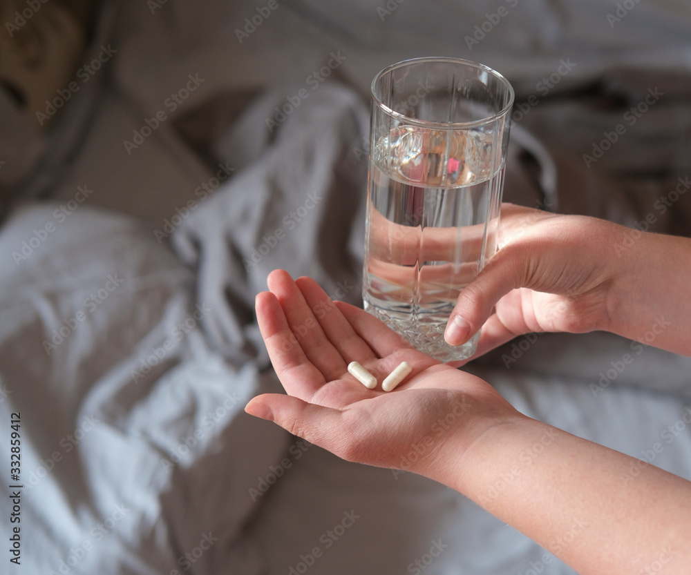 hands of young woman holding pills and glass of water and standind near bed. hands of young woman holding pills and glass of water and standind near bed.