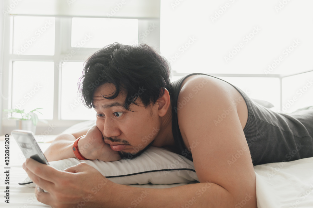 Sleepy Asian man is using smartphone while lying on the bed. Sleepy Asian man is using smartphone while lying on the bed.
