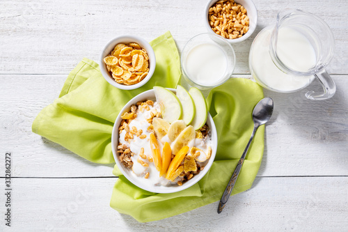 Granola and vegetarian yogurt with slices of apple, apricot, banana and a jug of milk on a white wooden background. Healthy breakfast concept. Top view