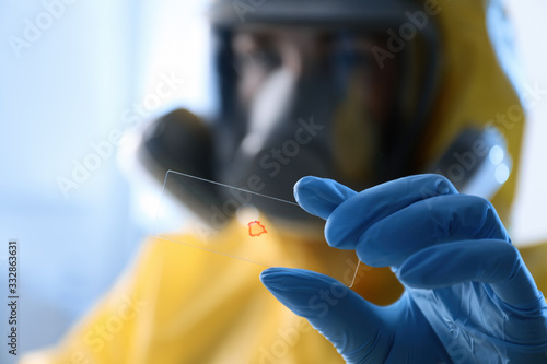 Scientist in chemical protective suit with microscope slide on light background, focus on hand. Virus research
