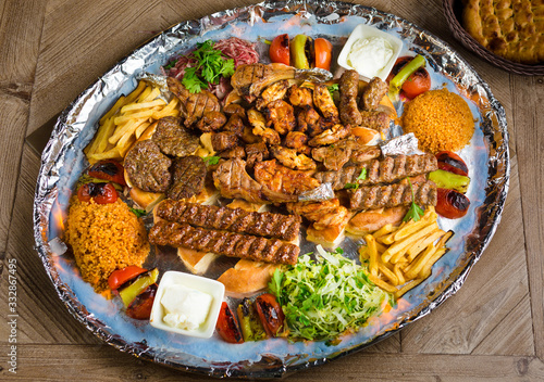 Full view of Persian Mix Kebab of minced meat and chicken With Rice and french fries and vegetables in a large traditional tray on wooden table